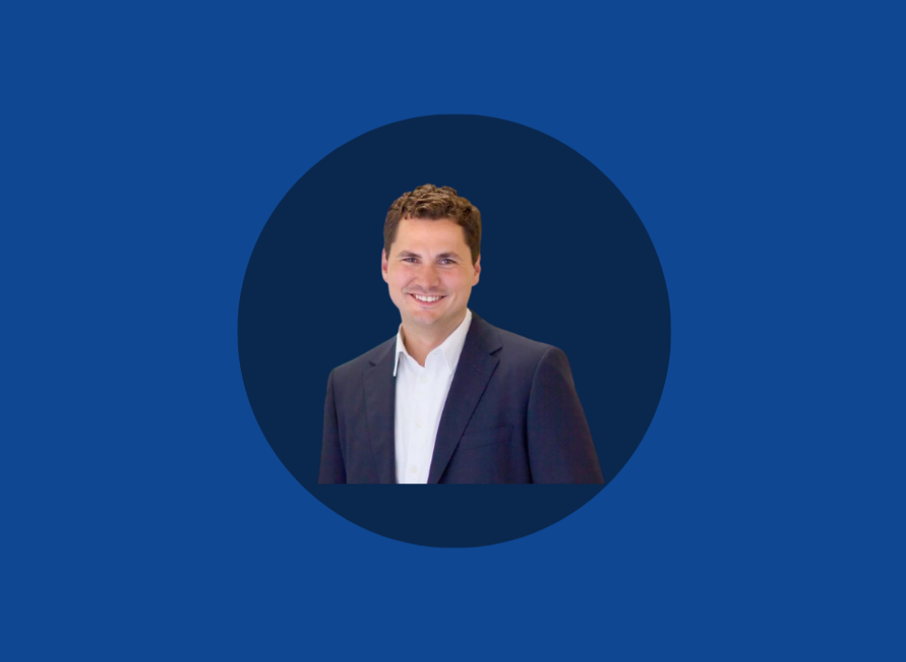 Smiling man in a suit with a white shirt, embodying the essence of hybrid working, captured in a circular frame on a blue background.