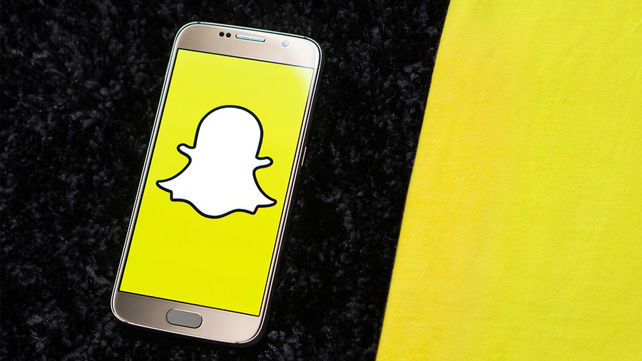 A smartphone displaying the Snapchat logo on its screen is placed on a black surface next to a bright yellow fabric, illustrating how modern tools can enhance HR efficiency.
