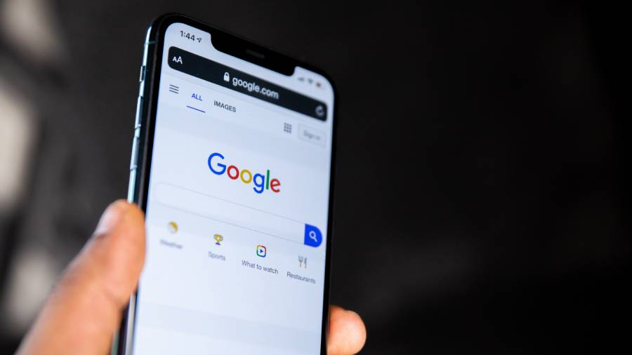 A hand holds a smartphone displaying the Google search homepage against a dark background, symbolizing how easily accessible tools can aid in People Management and Human Resources tasks.