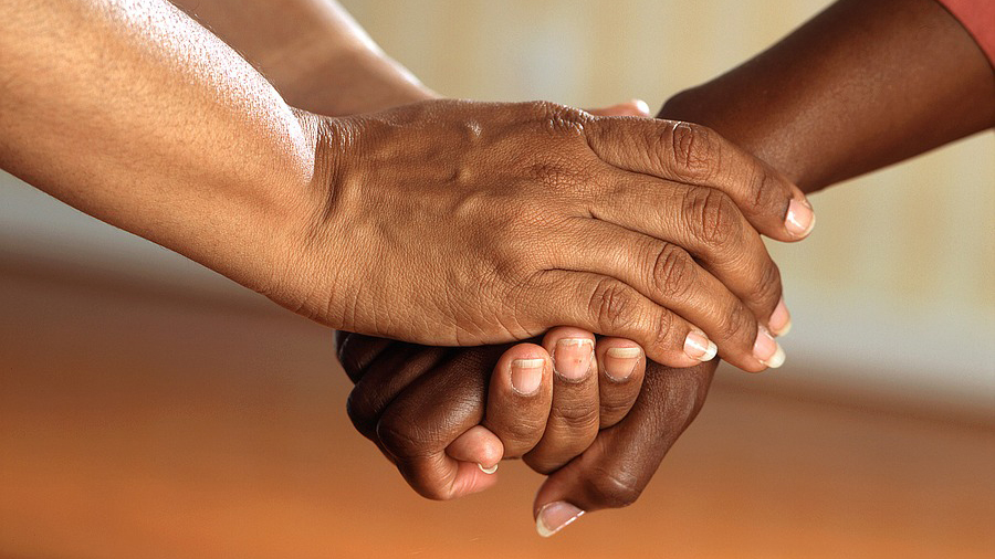 Close-up of two pairs of hands clasped together, symbolizing the support and connection integral to effective people management.