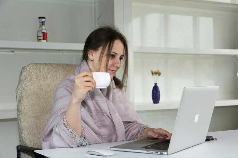 An older woman sitting at a desk with a laptop and a cup of coffee.