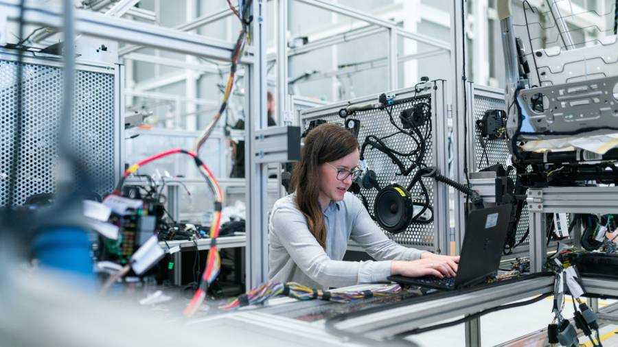 A person works on a laptop in a high-tech laboratory setting, managing personnel and coordinating human resources amidst the wiring and machinery components.
