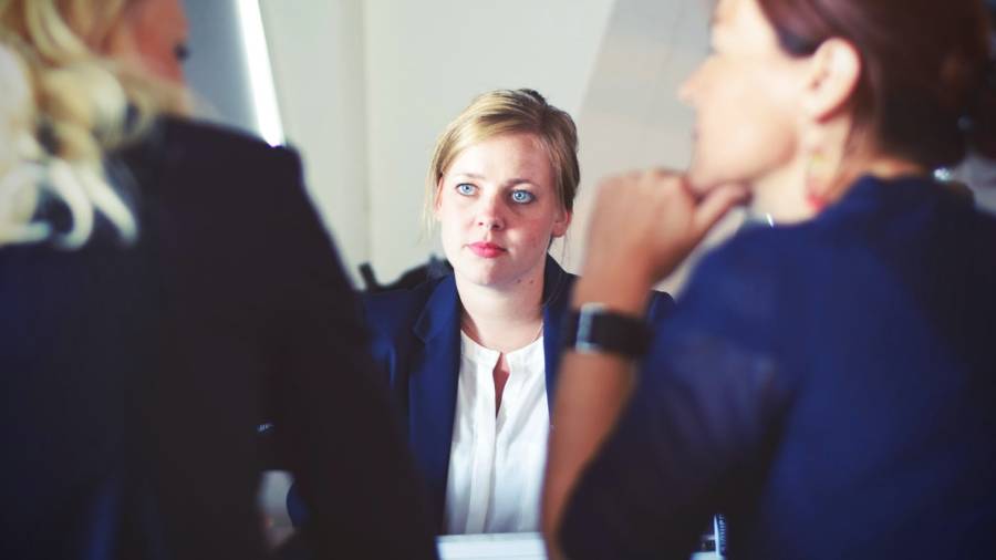 Three people in business attire are sitting at a table, engaging in a discussion. The person in the middle, possibly an HR professional, is attentively listening to the others.