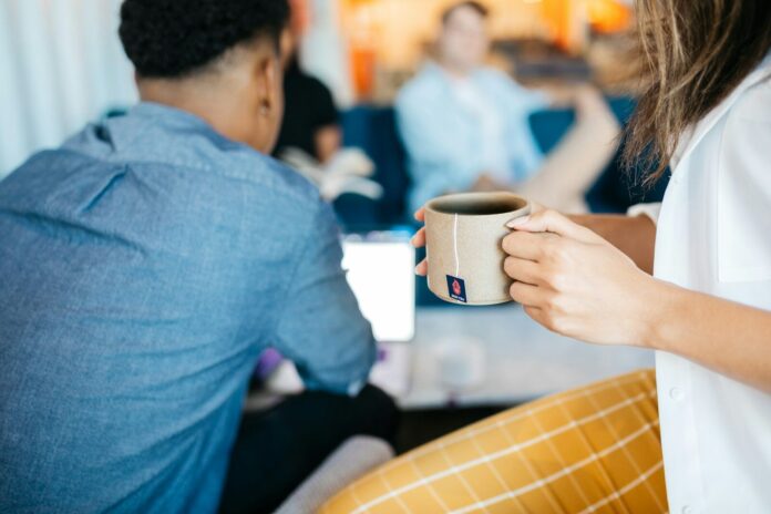 Photo by Zest Tea A woman holds a mug of coffee at an office.
