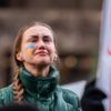 Ukrainian woman with a small Ukrainian flag painted on her cheek, with STOP Putin banner behind her