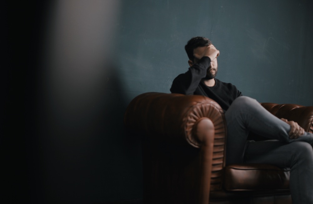 A person sits on a leather couch with one hand covering their face, showing a gesture of frustration or fatigue, seemingly overwhelmed by the great resignation.