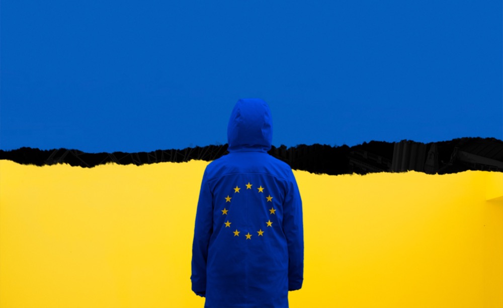 A person wearing a blue jacket with the EU flag faces a backdrop resembling the Ukrainian flag, symbolizing solidarity amidst the war on Ukraine.