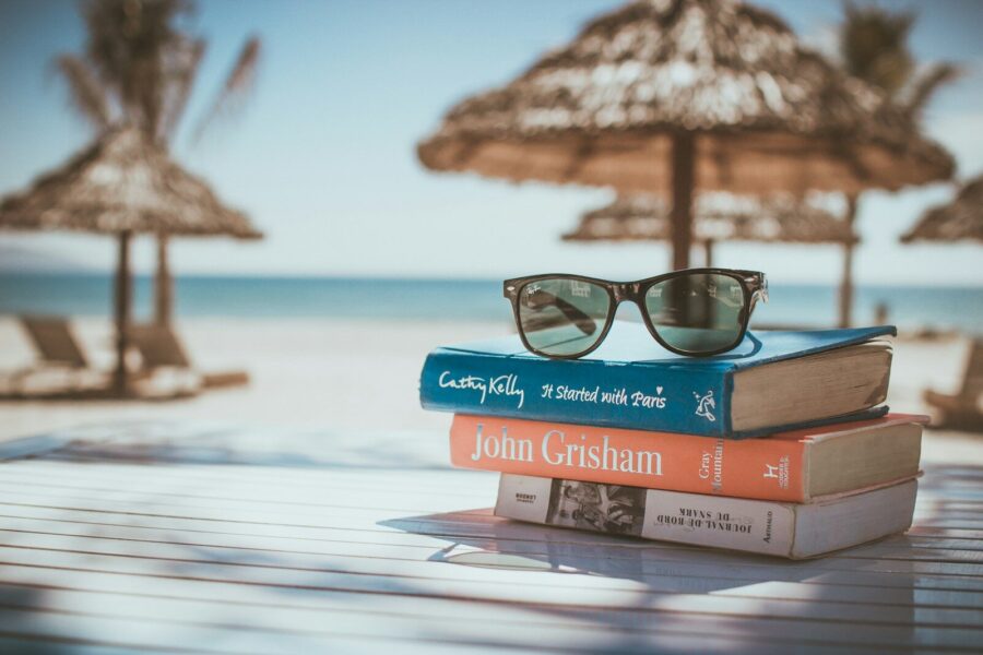 Sunglasses on top of a stack of books on a table by the beach.