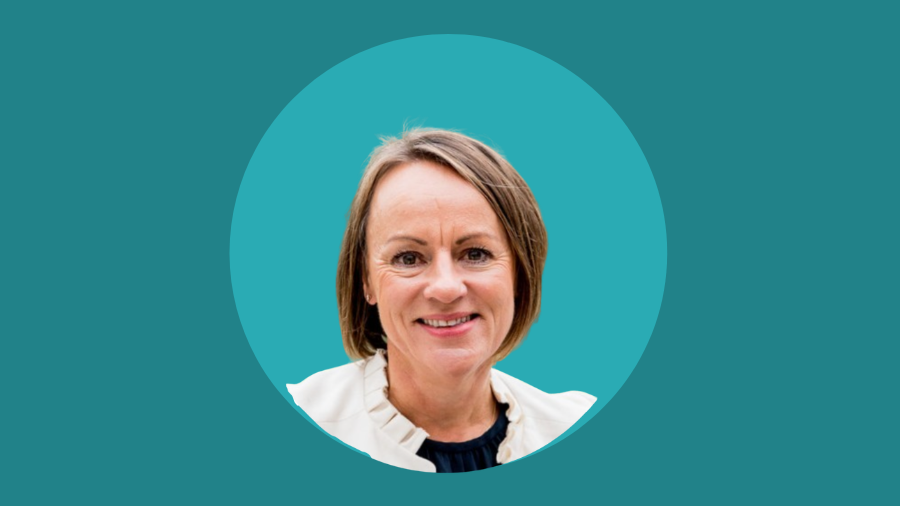 A woman with short brown hair and a white blouse is smiling in a headshot against a teal background, embodying the positive spirit of a gender-inclusive workspace.