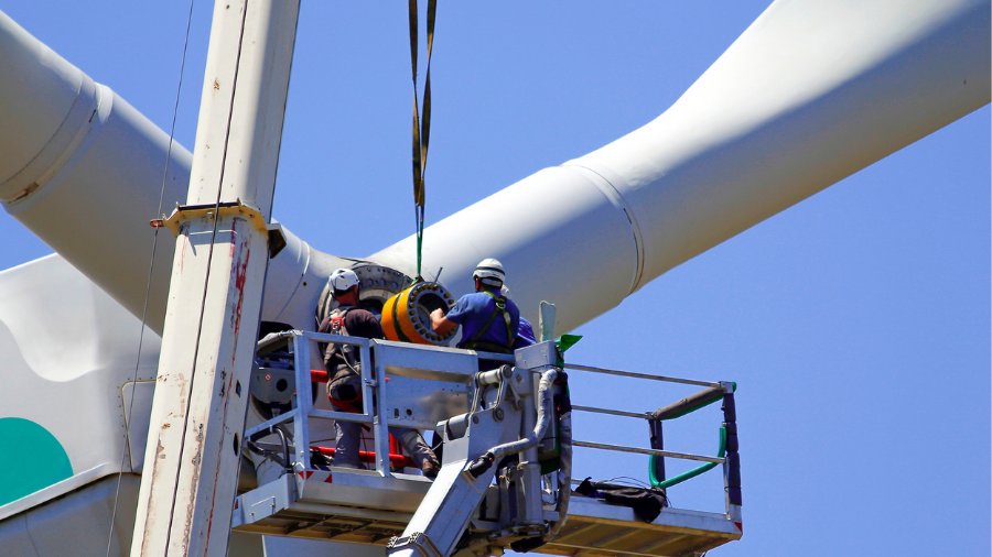 Two workers in safety gear repair a wind turbine using a crane lift, exemplifying the growth of green jobs in the renewable energy sector.