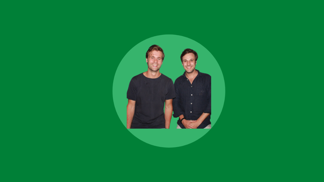 Two men are standing and smiling in front of a green background. They are casually dressed, embodying the relaxed spirit of innovators in the technology industry.