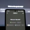 A smartphone displays an AI chatbot in front of a computer screen.