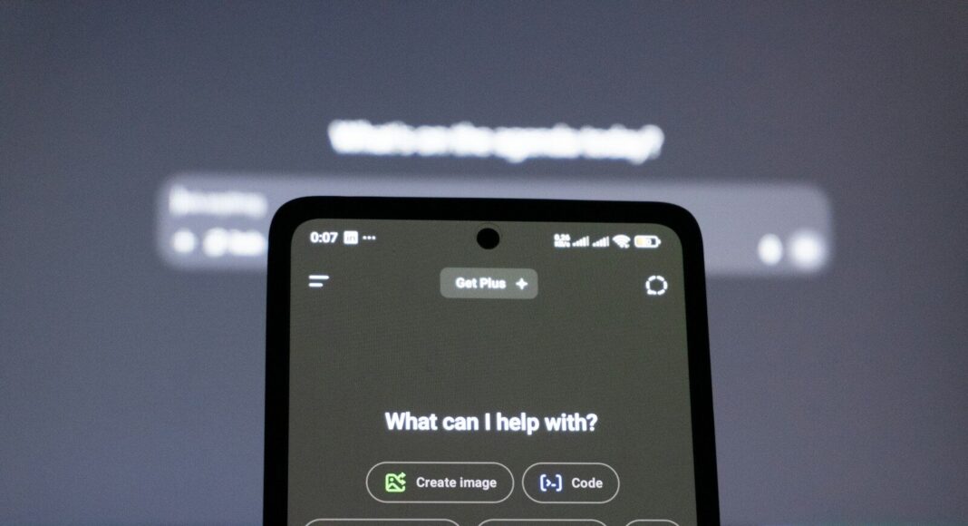 A smartphone displays an AI chatbot in front of a computer screen.