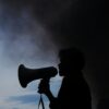 A silhouette of a man holding a megaphone in front of a cloud of smoke.