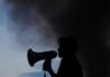 Whistleblowing reports ‘surge by up to 250 percent’ at councils as new rights take effect A silhouette of a man holding a megaphone in front of a cloud of smoke.