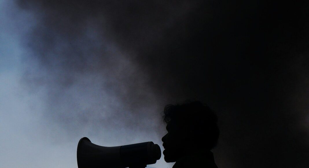 A silhouette of a man holding a megaphone in front of a cloud of smoke.