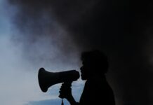 Whistleblowing reports ‘surge by up to 250 percent’ at councils as new rights take effect A silhouette of a man holding a megaphone in front of a cloud of smoke.