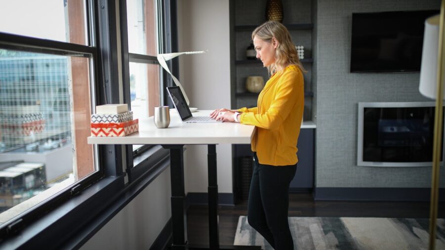 A woman works on a computer at a standing table in an office.